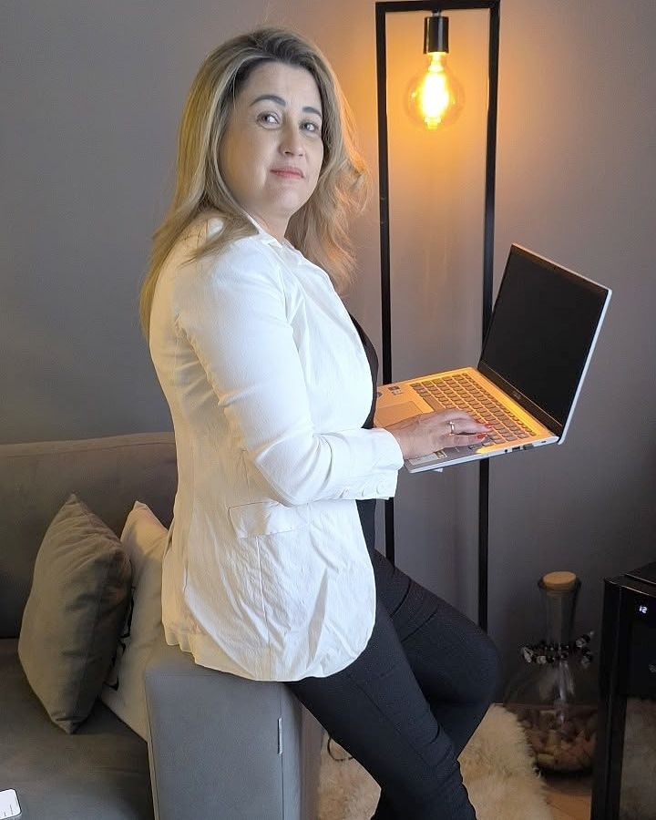 Adriana Silva sentada en el brazo de un sofá, con la notebook abierta en la mano.